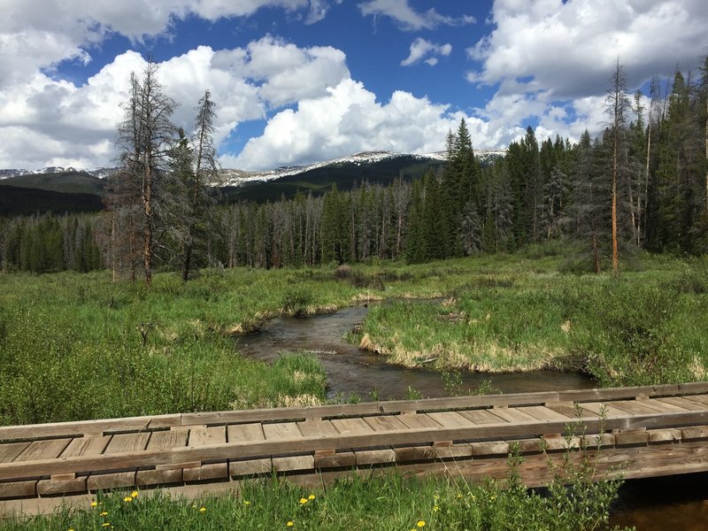 Bridge crossing with meadow and Indian Peak views.