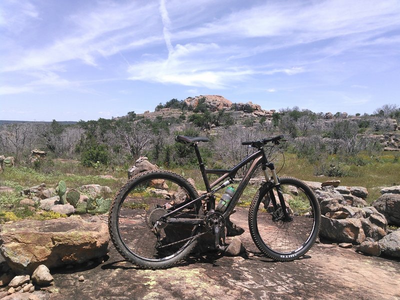 Solid granite trail weaving through boulders and prickly pear cactus along the RPR Loop with Reveille Peak in the background.