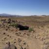 Cow laying on Coyote Pass saddle. View of Tech Ridge area of Foothills Rim & Monolith Gardens Trail across the highway.