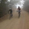 Riders pedal the dirt road on a foggy morning.