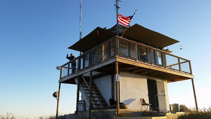 The custodian of the lookout tower waves good bye on a sunny evening.