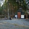 a look at hte whole rest stop area, grill hut & log bench, garbage can on behind the logbench.