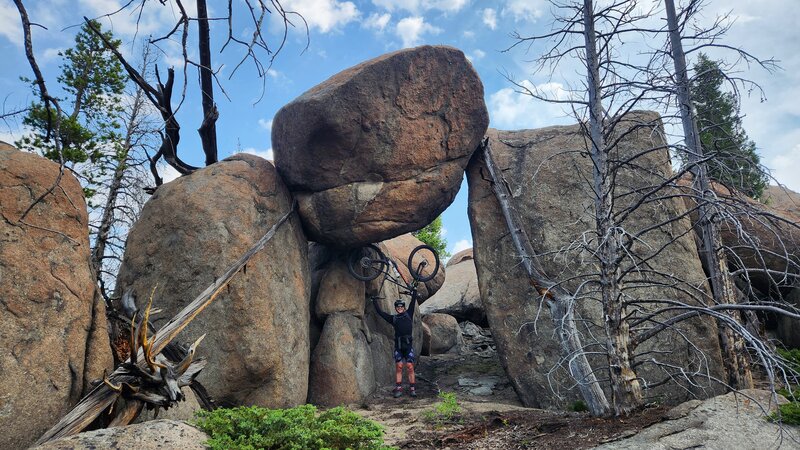 A mountain bike rider uses his bike as a shield against being crushed by a massive boulder.