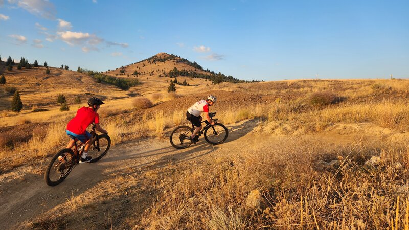 Two riders ride up the banked turns of the Bike Park Perimeter Trail.