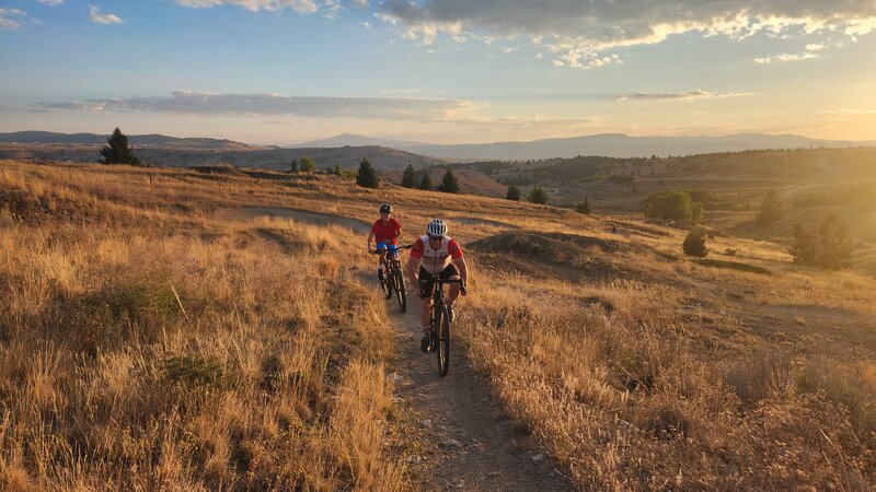 Two riders riding up the banked turns of the Butte Bike Park Perimeter Trail.