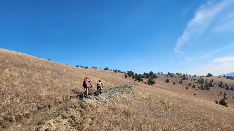 Two riders head east on the Tin Can Nellie Trail towards the top of the ridge.