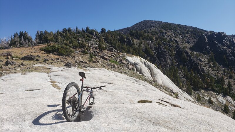 A mountain bike balances by itself on the white rock slabs with the summit of Elkhorn Peak in the background.